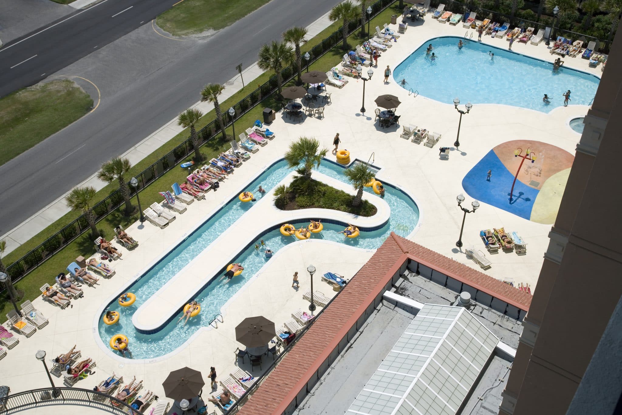 An aerial view of a large outdoor pool area with people swimming and lounging on chairs.