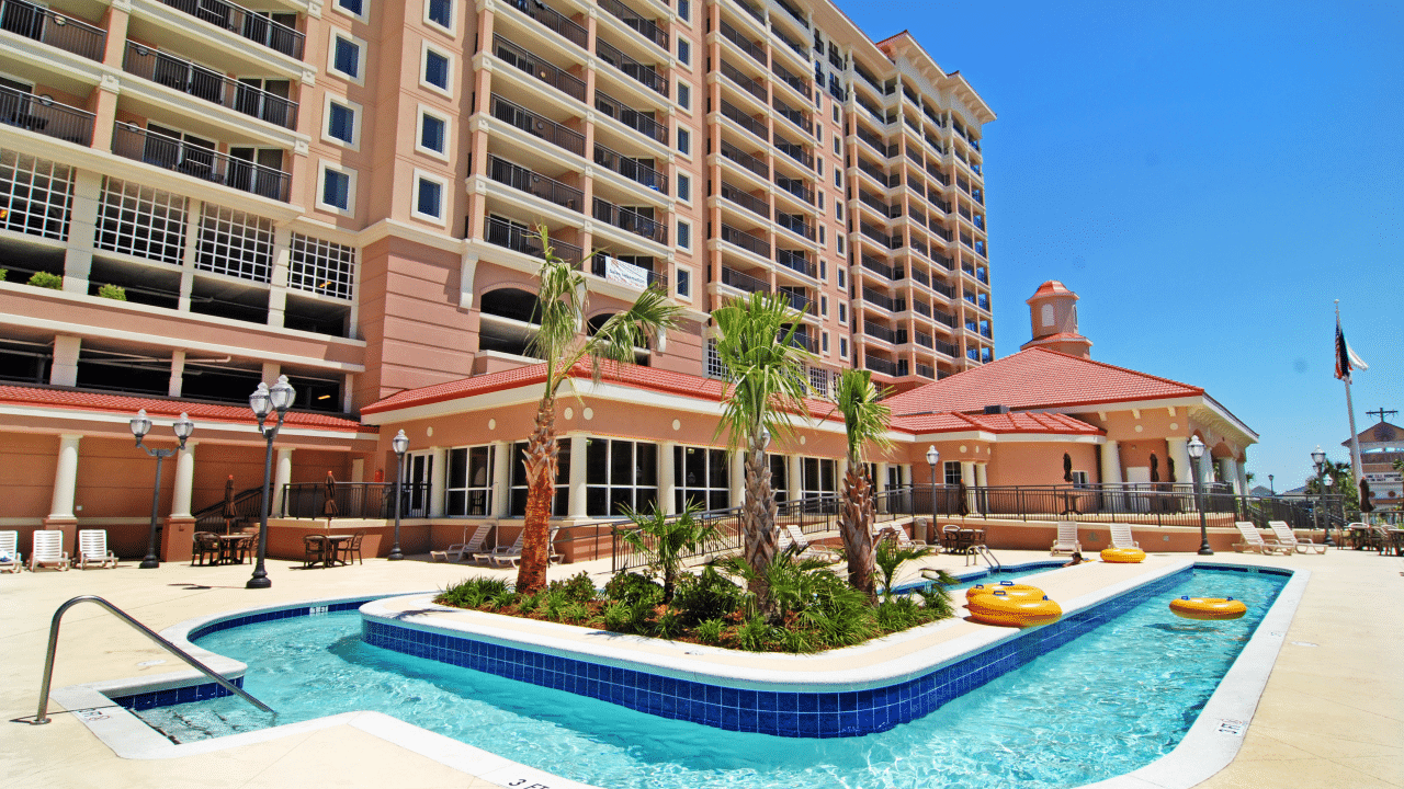 A large hotel building with a pool and palm trees in front of it.